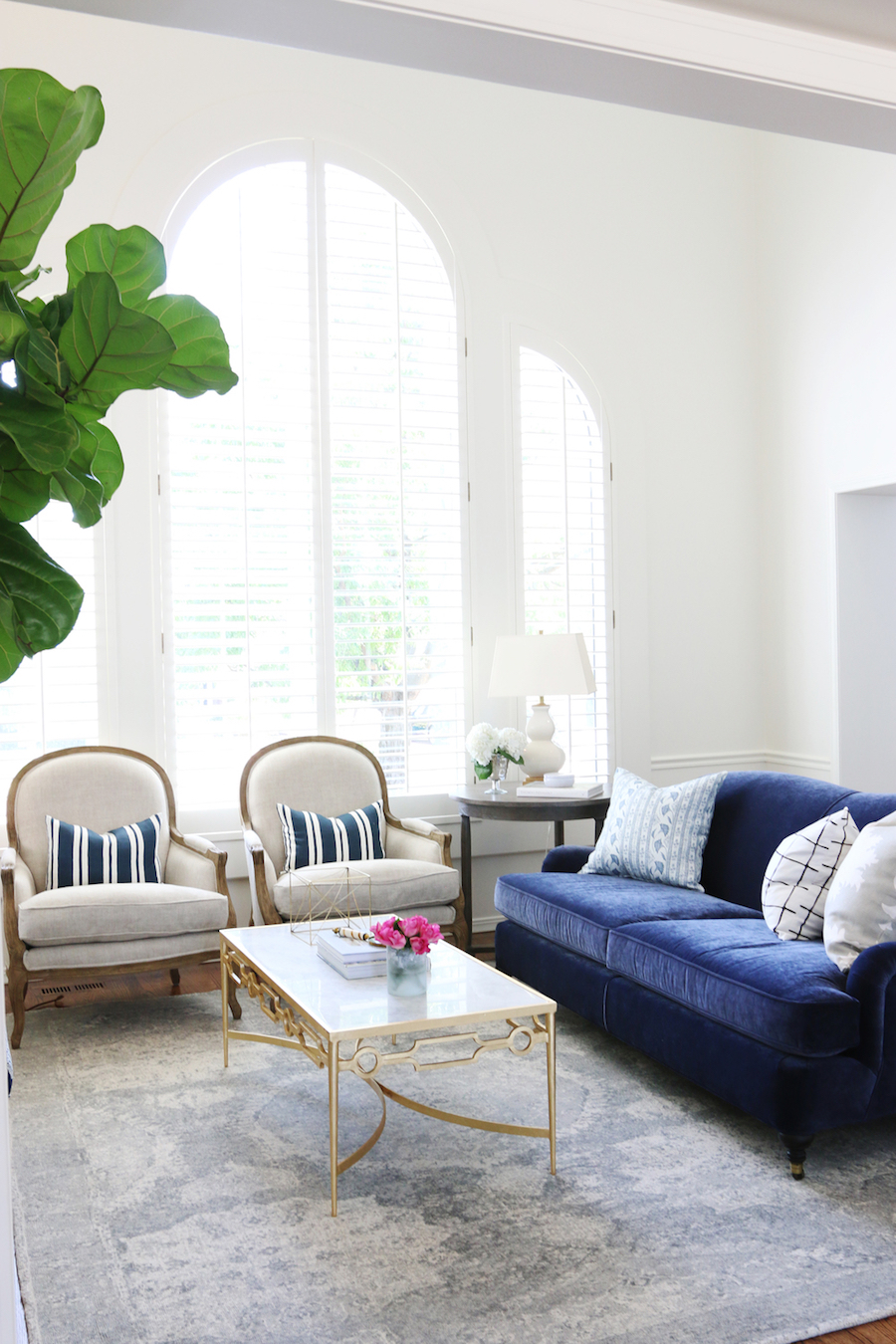 Blue velvet sofa with two white chairs and a grey rug