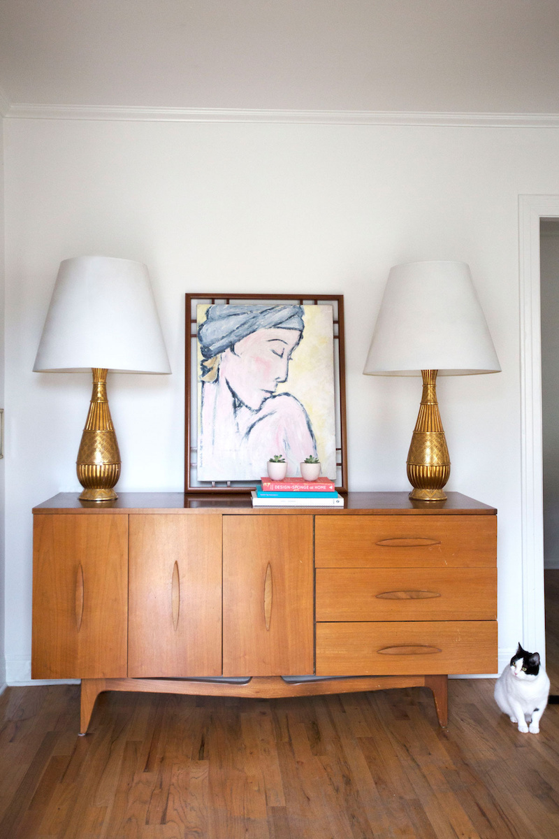 Claire Zinnecker Wooden sideboard and golden lamps with art