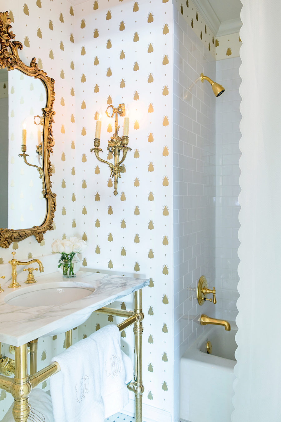 Gold fixtures in marble bathroom with gilded mirror and spotted wallpaper