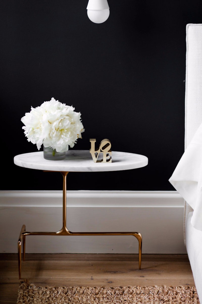 White marble nightstand table with brass base against black wall via Tamara Magel