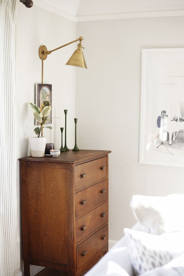 Brass swing arm sconce above wood dresser in bedroom via cocokelley