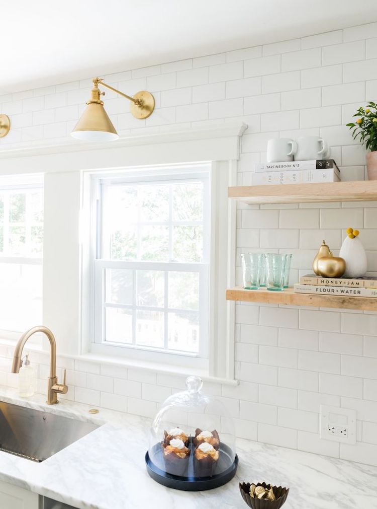 White kitchen with brass sconces and subway tiling and marble counter