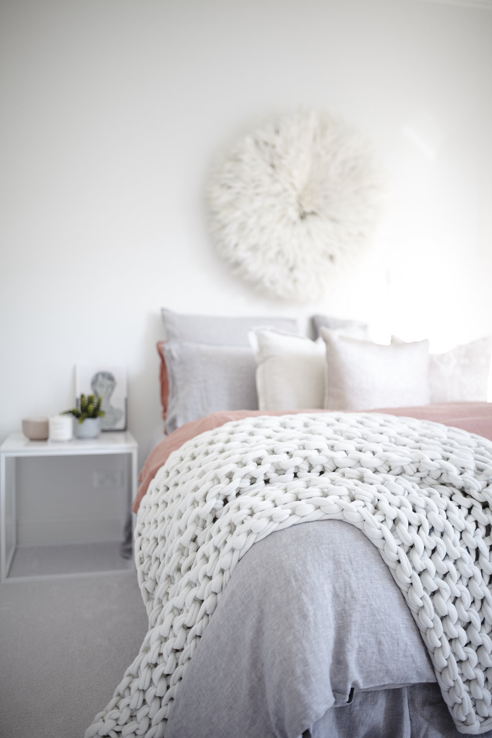 Bedroom with white knit blanket and feather wall decor