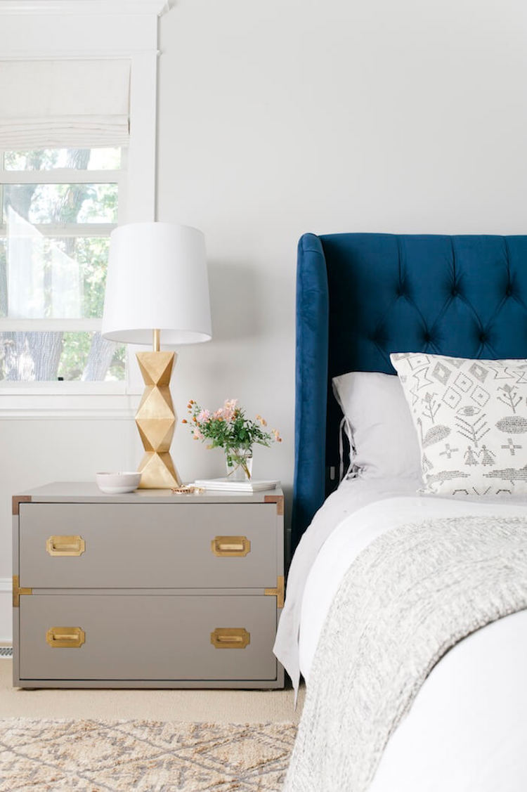 Gold table lamps in bedroom with navy blue tufted headboard