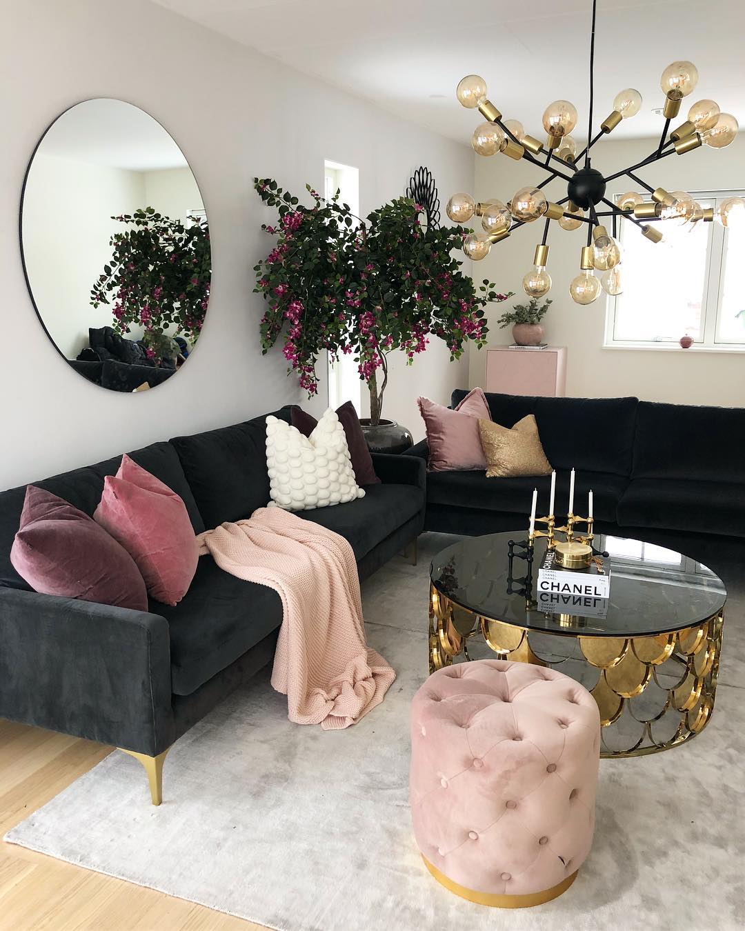 Dark gray sofa with beige rug, pink tufted stool, and glass coffee table via @interiorbyvanessa