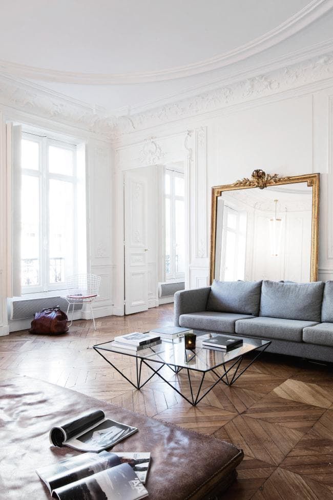 Parisian living room with gray sofa and leaning wall mirror via vogue australia