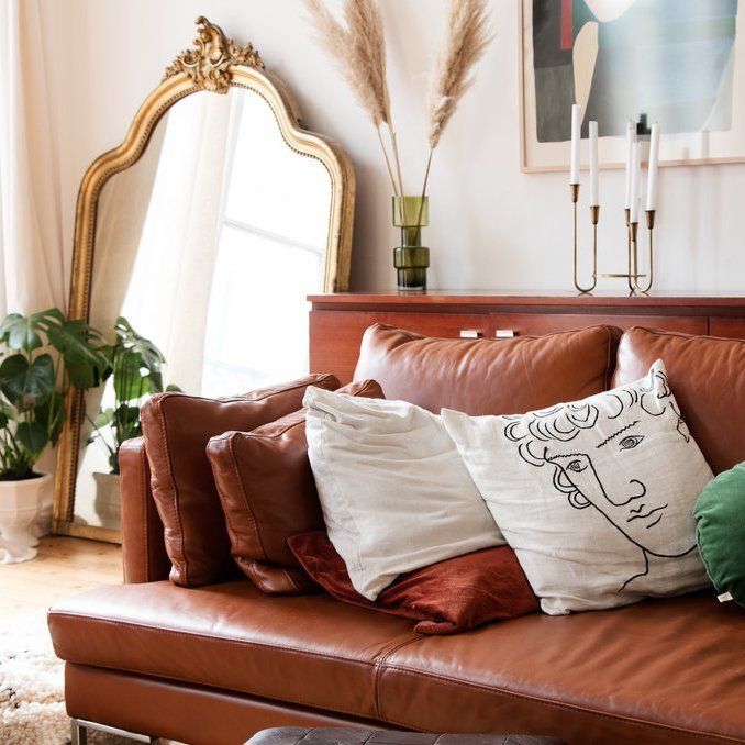 Parisian living room with brown leather sofa and gold leaning wall mirror via Adenorah