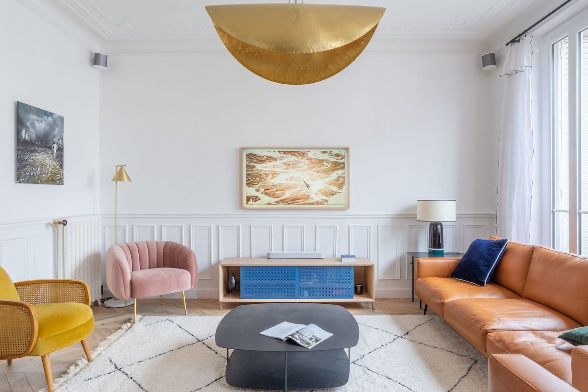 Parisian living room with brown leather sofa, pink and yellow accent chairs via Quitterie de Pascal