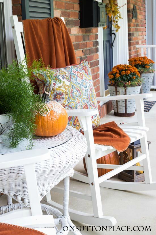 Fall front porch with orange throw blanket on a white rocking chair via onsuttonplace