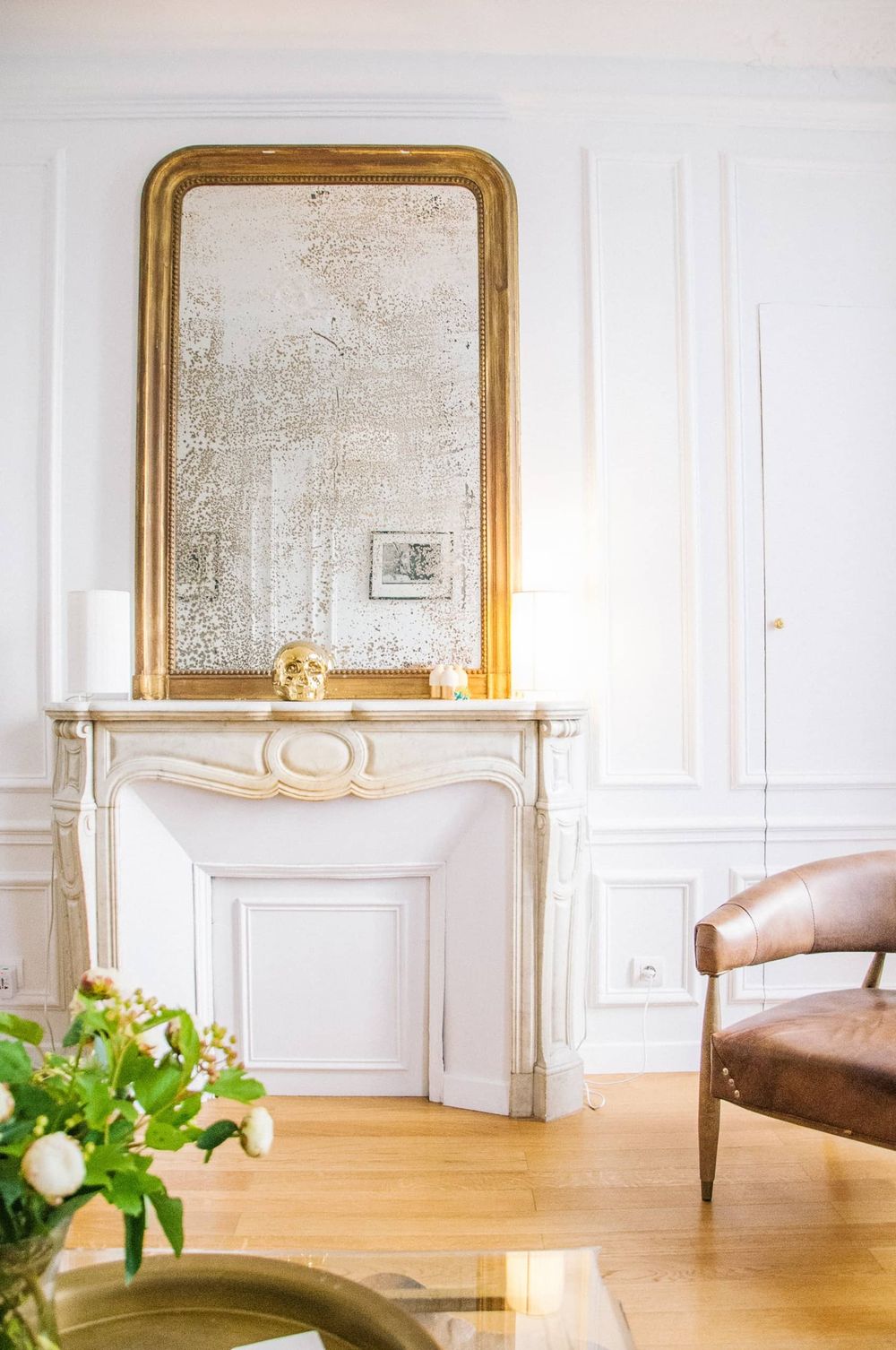 Parisian fireplace with distressed mirror and brown leather chair via Katy Cartland