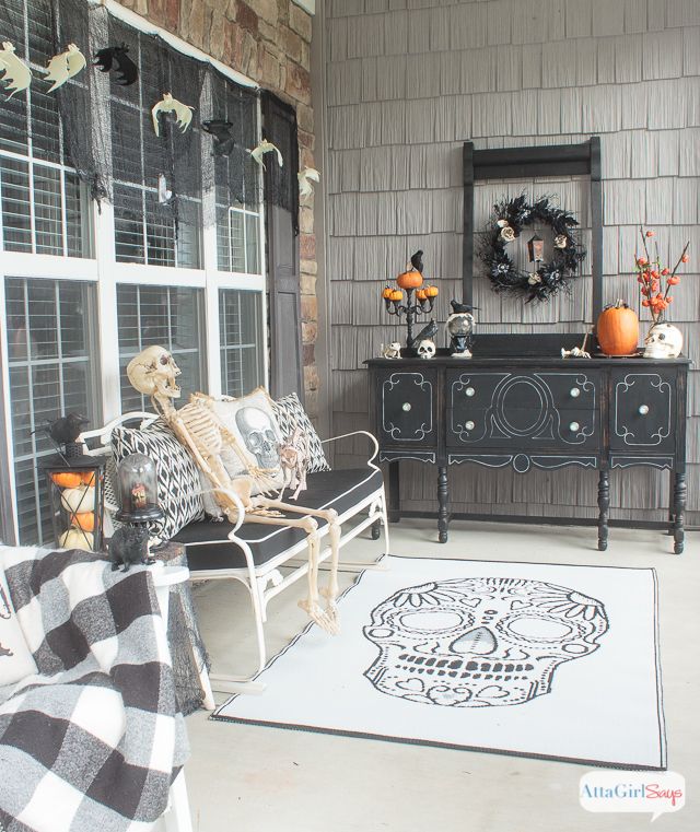 Skull rug on Halloween front porch with skeletons on bench and black cushions