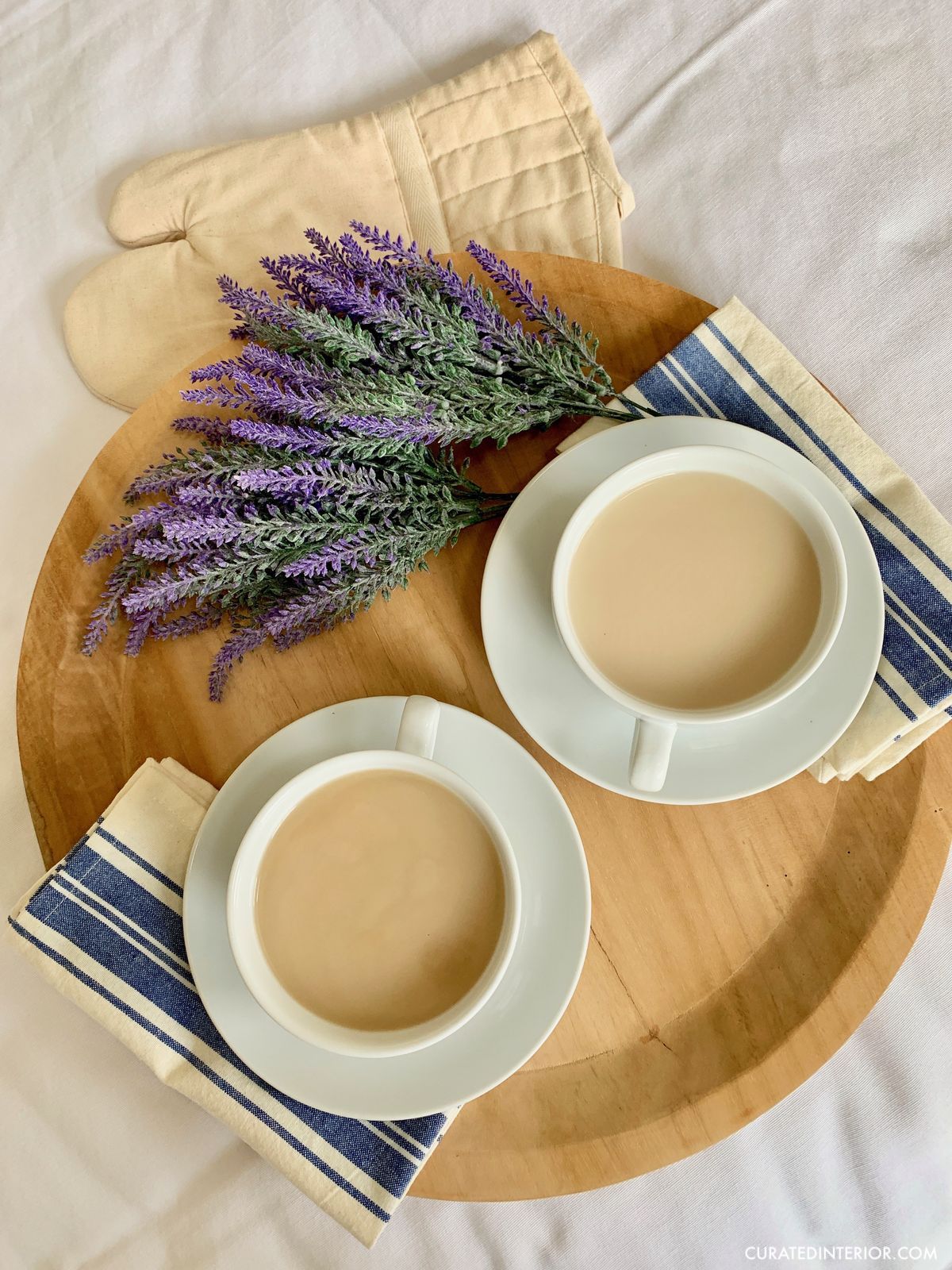 French country coffee bar essentials - oversized coffee cups and saucers, mango wood tray, blue and white striped napkins, lavender stems, and organic cotton oven mitt