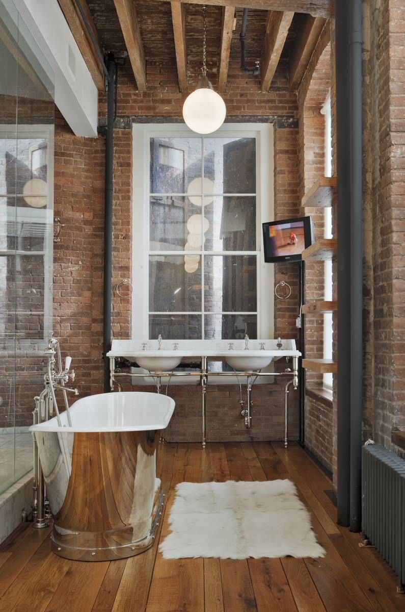 Brick walls in an industrial loft nyc bathroom with a silver bathtub via Jane Kim Design NY
