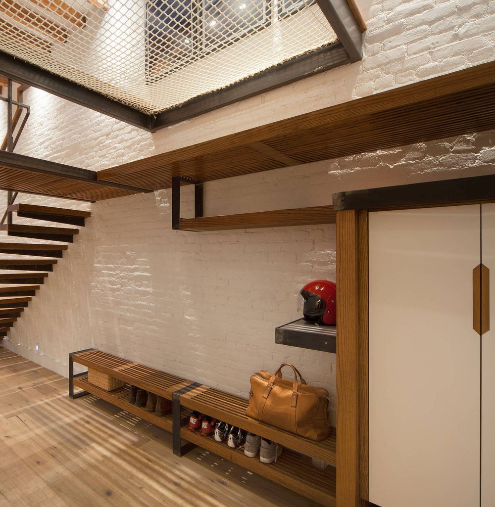 Industrial Entryway Design with Painted White Brick Wall Below Floating Staircase via Arjune Design