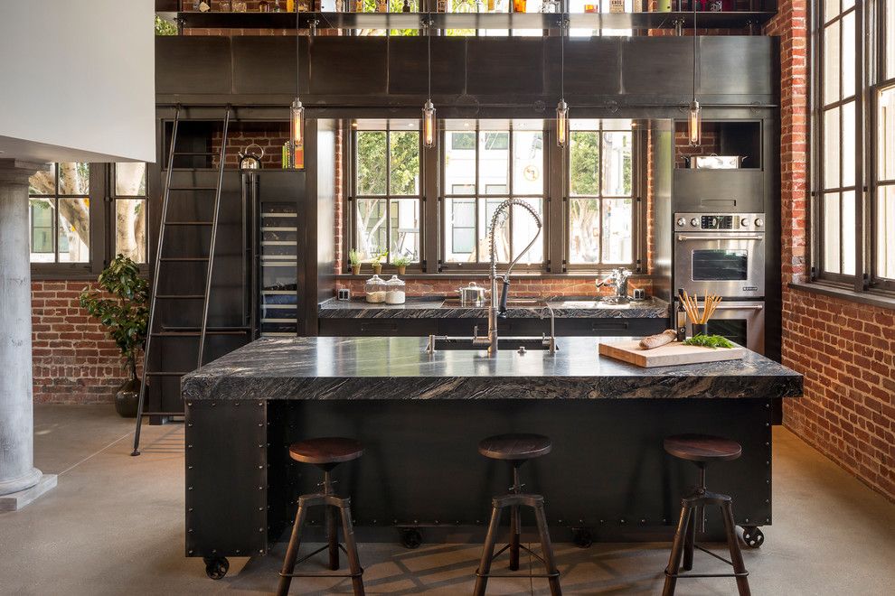 Ladder in Industrial eat-in kitchen design with steel cabinets, black marble countertops, stainless steel appliances, undermount sink in Clocktower Loft San Francisco via Muratore Construction