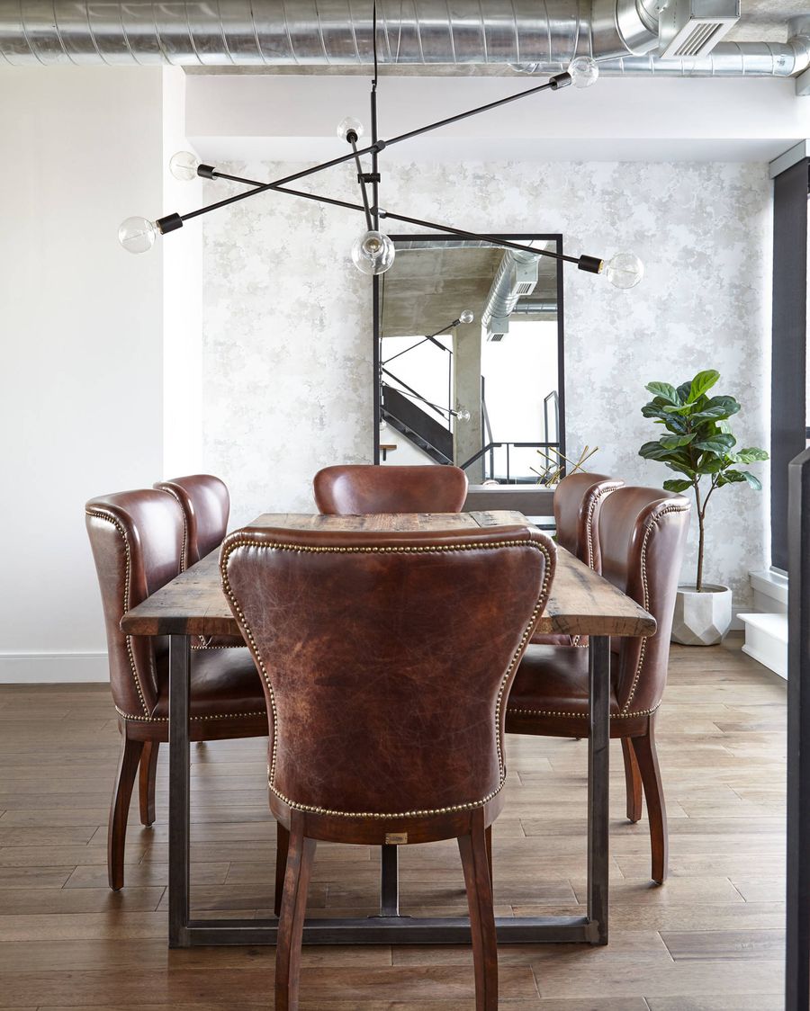 Chaises à manger en cuir et lustre à tige noire dans une salle à manger industrielle